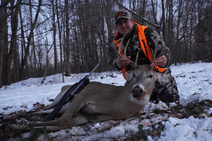 Hunter with harvested whitetail buck in snowy woods