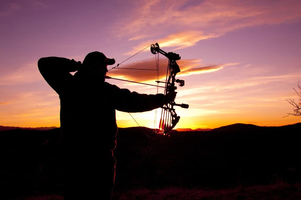 Bowhunter at full draw silhouetted against an Oregon sunset—hunting culture on the line if IP28 passes